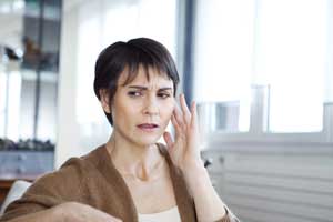 A woman is sitting down, touching her ear in pain.