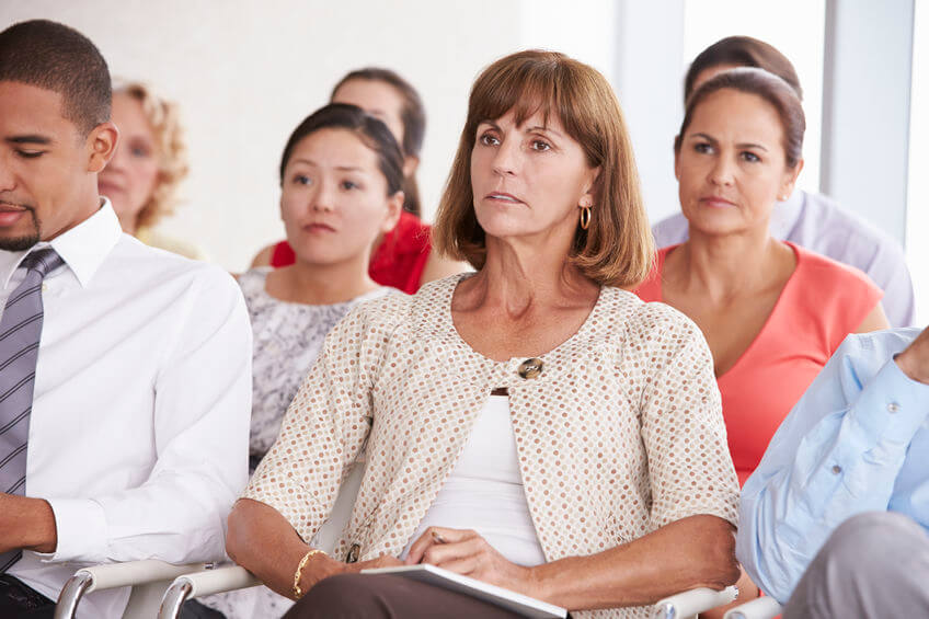 A woman in a conference room struggles to hear a person speaking.